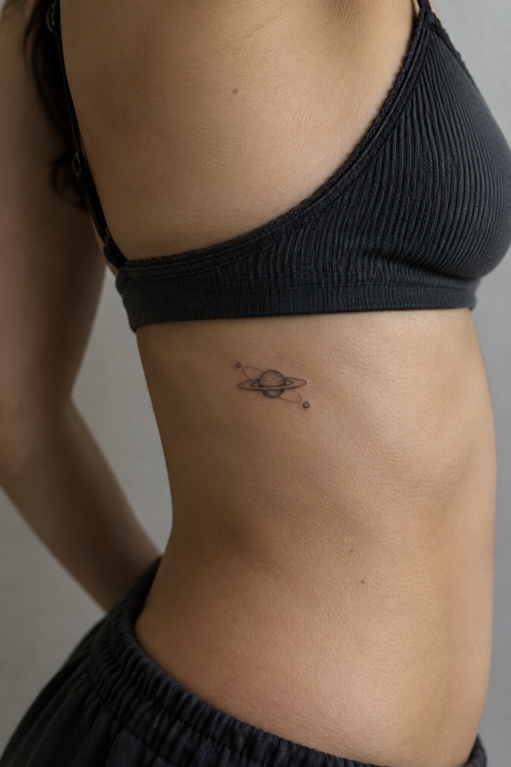 Minimalist Saturn tattoo on midriff below black ribbed crop top