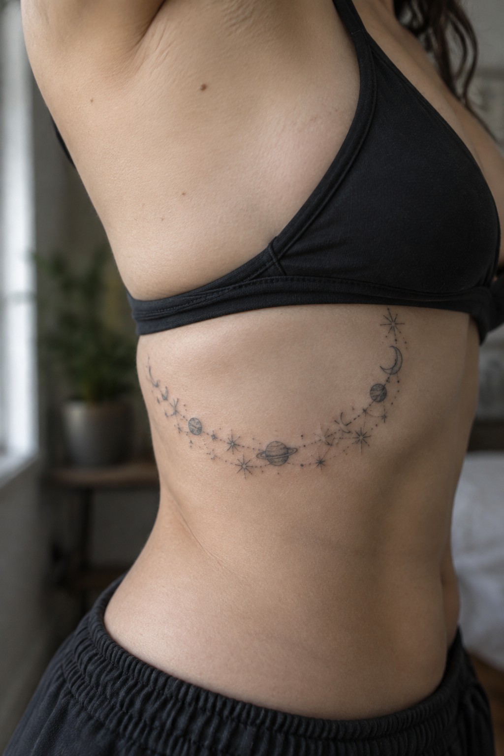 Woman's torso with black sports bra and curving celestial tattoo on ribs.