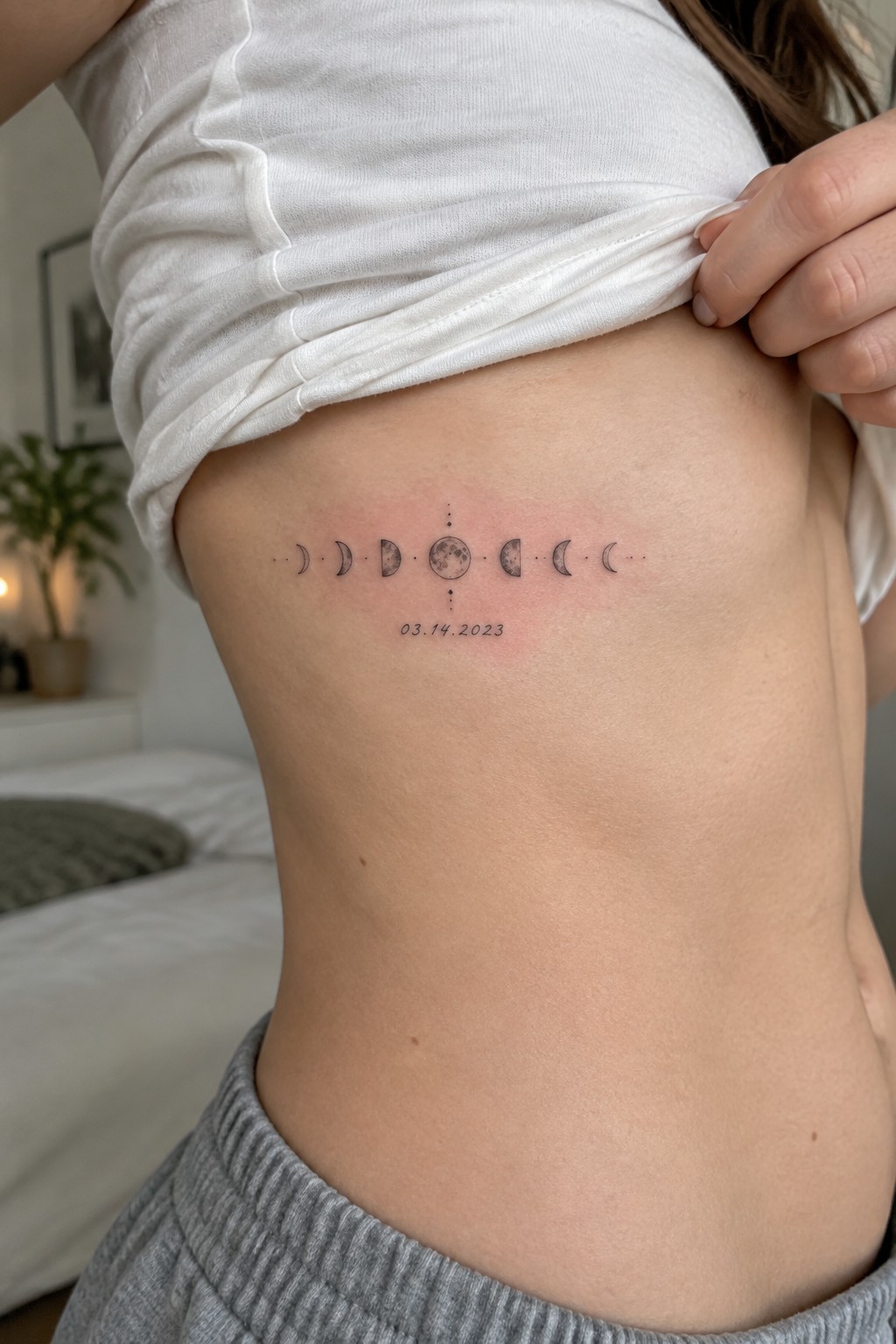 Fine line moon phases tattoo on ribs showing lunar cycle with full moon center and date below