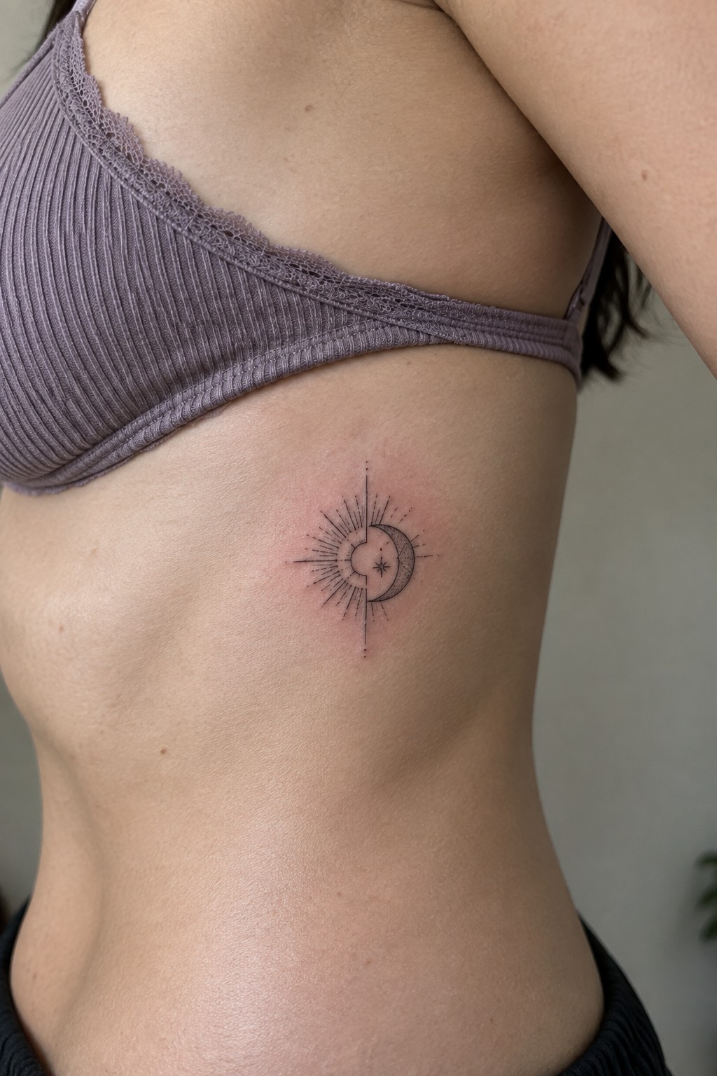 Purple ribbed bra above black sun-moon tattoo on ribcage skin