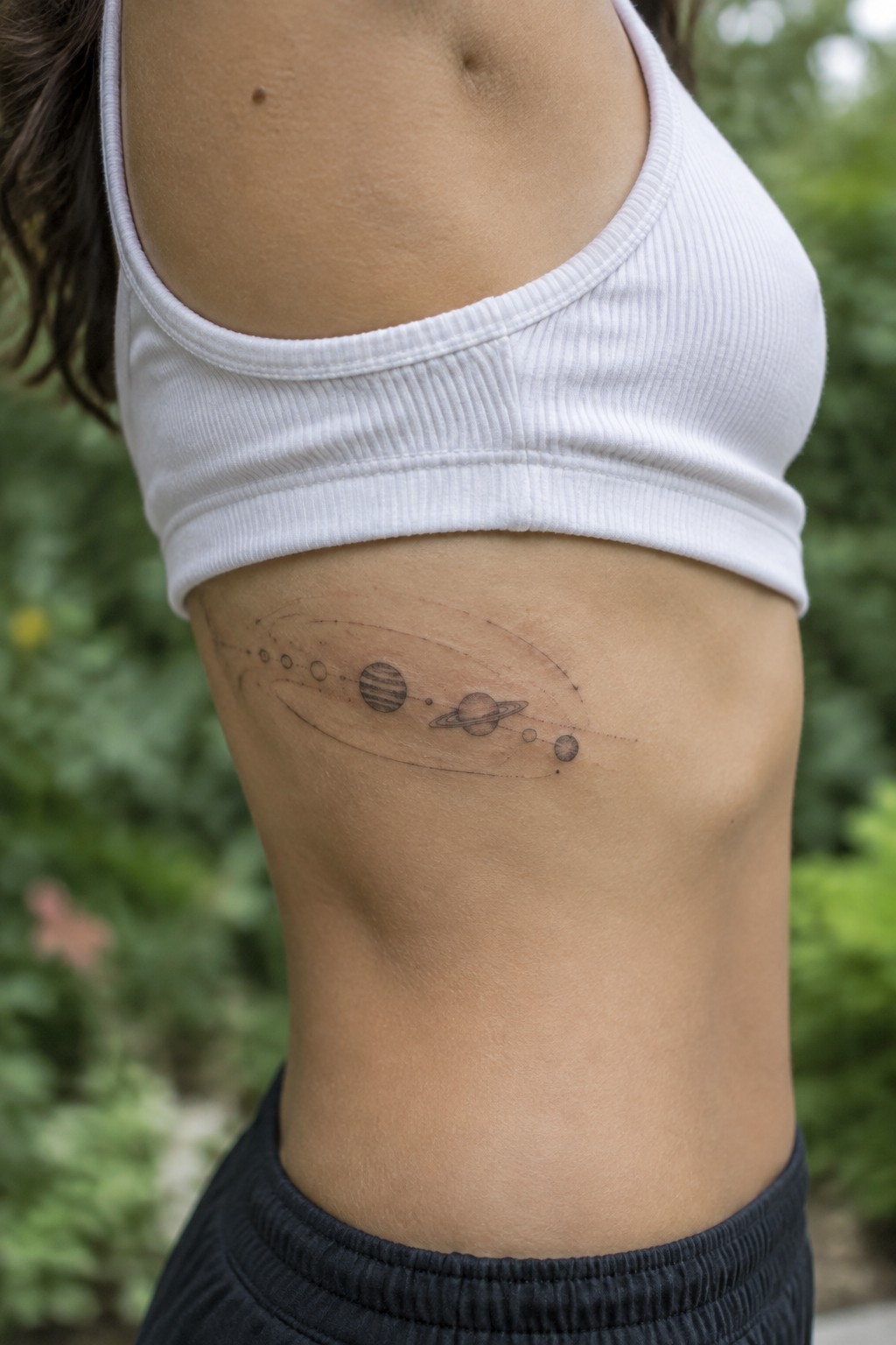 Solar system tattoo on side of torso below white crop top
