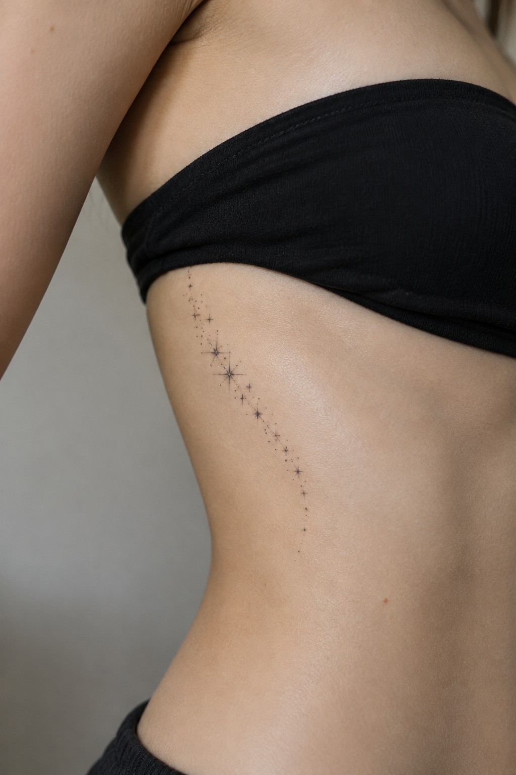 Black bandeau top with delicate star constellation tattoo curving down torso