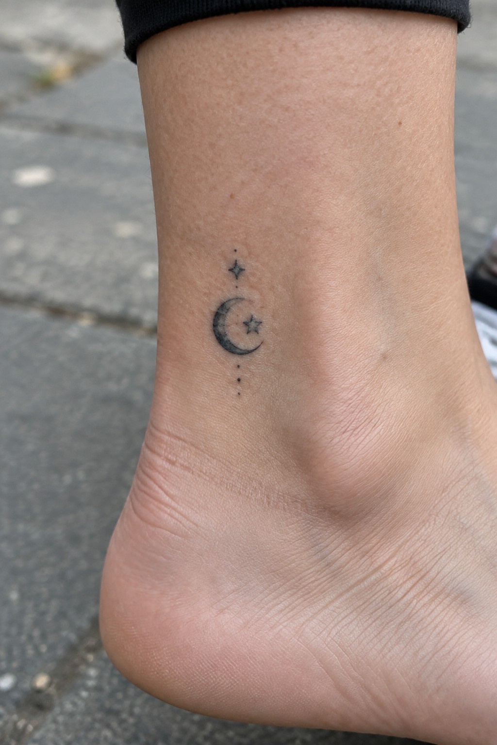 Black crescent moon and stars tattoo on light-skinned ankle with black cuff