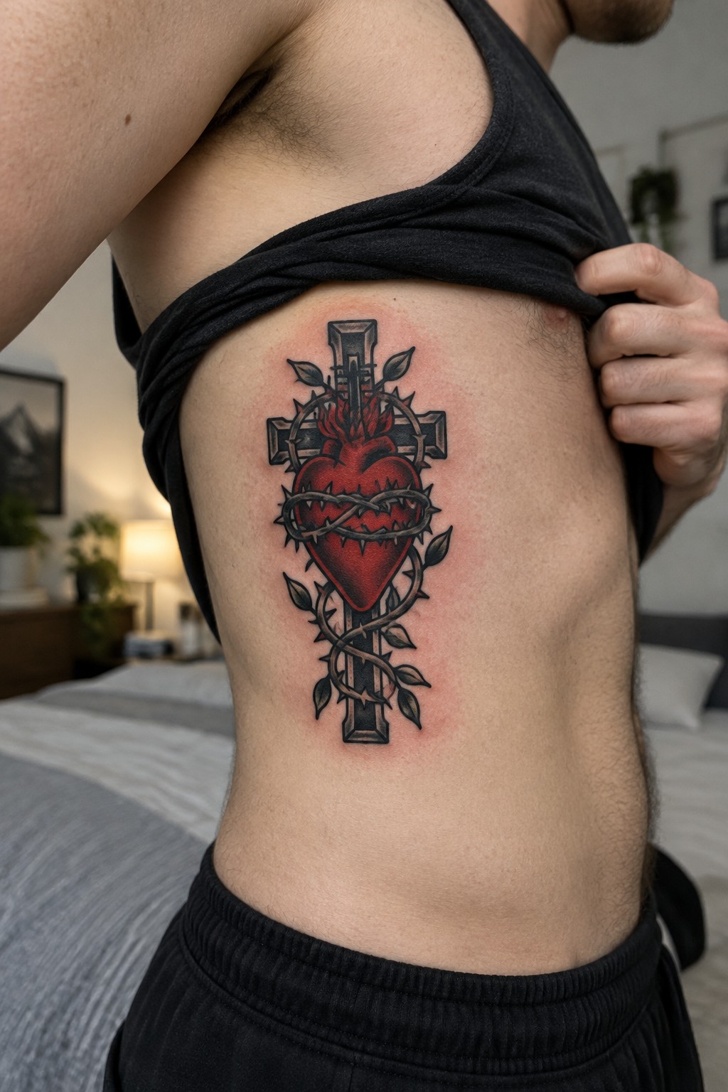 Man lifting black shirt to show red heart-cross tattoo with barbed wire on side
