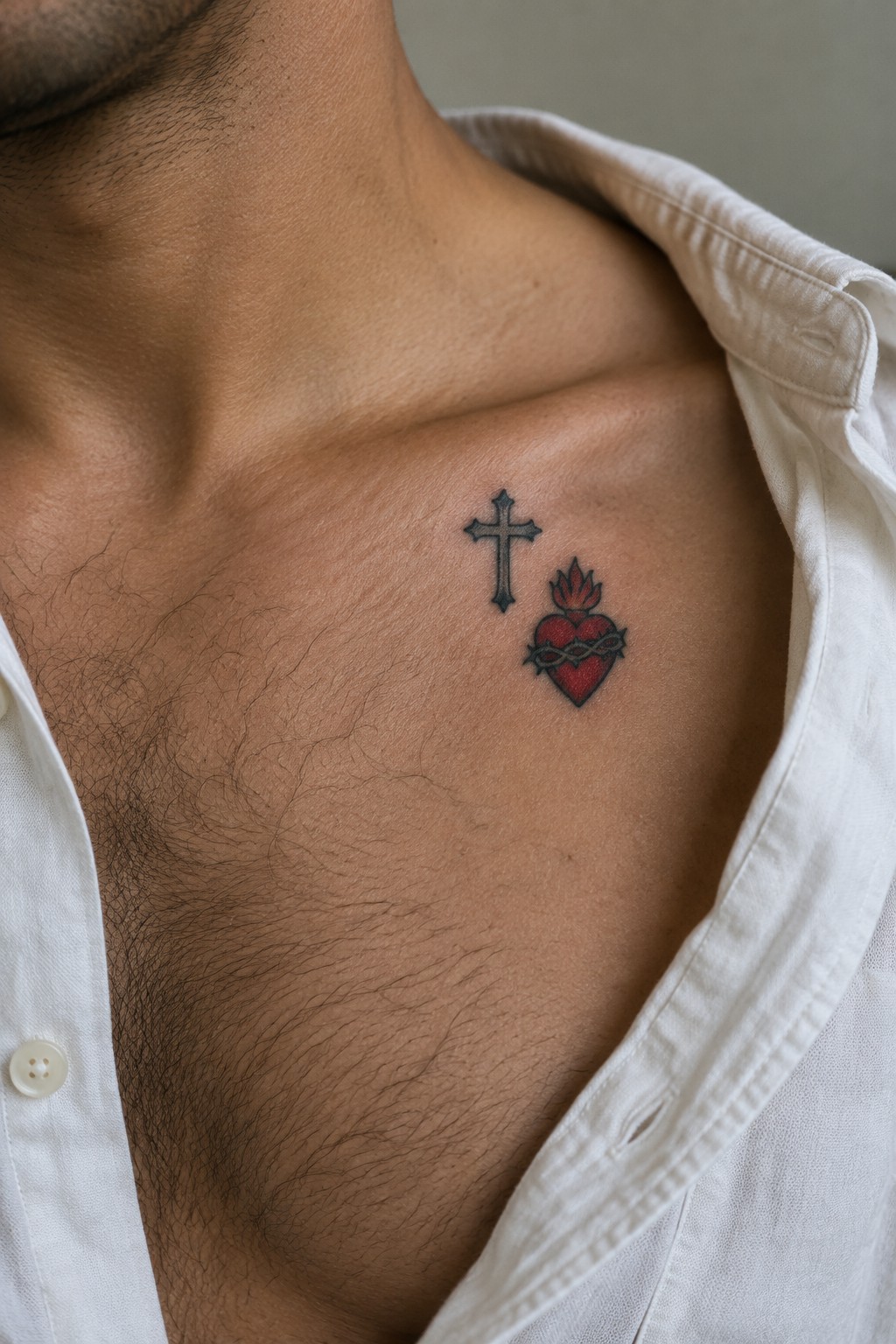 Small American traditional tattoo showing a black cross above a red sacred heart with thorns on a man's upper chest.