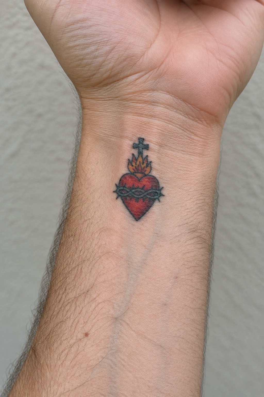 Traditional tattoo of flaming red sacred heart with cross and thorns on wrist.