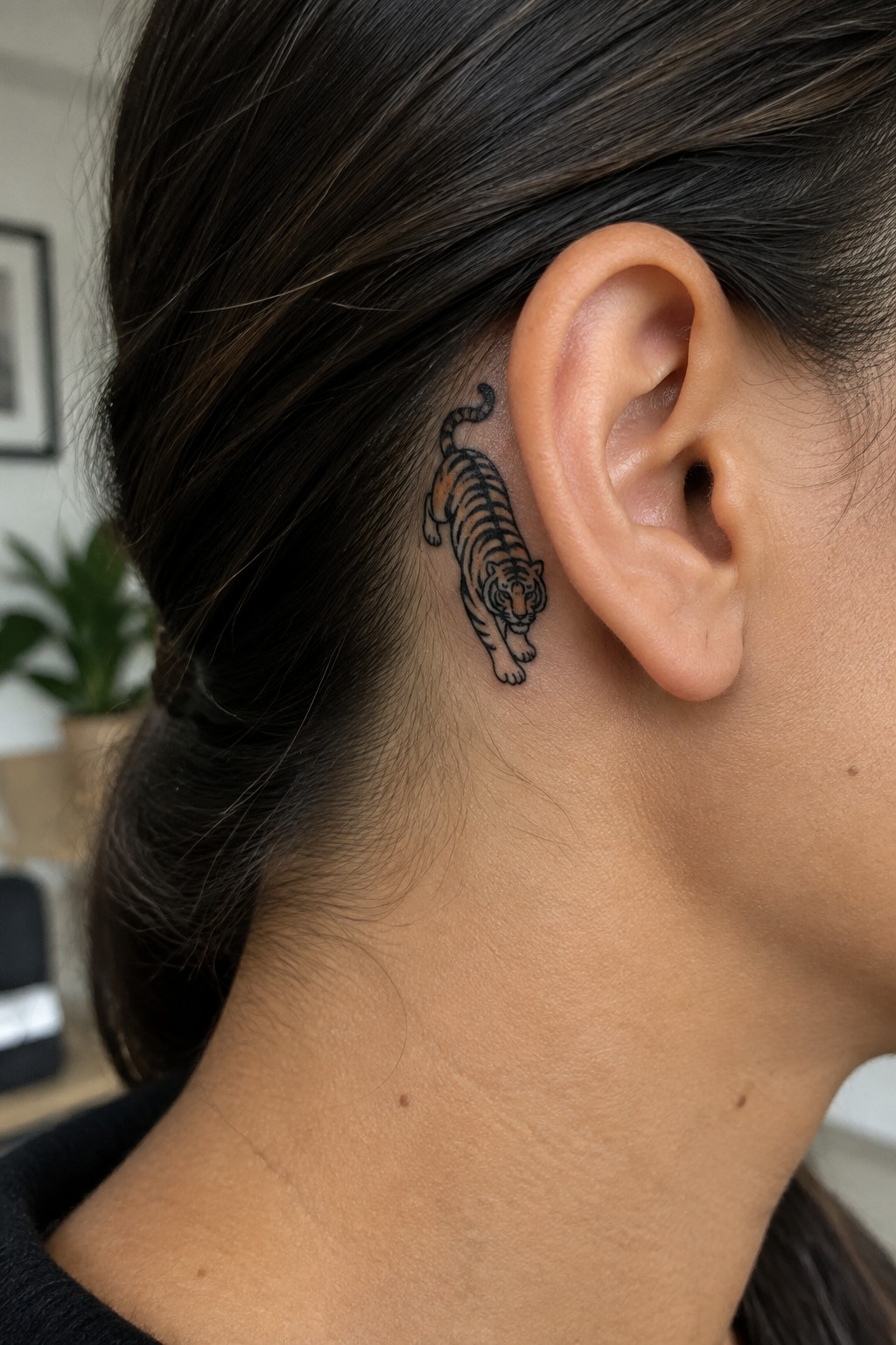 Tiger tattoo with orange accents behind ear on dark-haired person.
