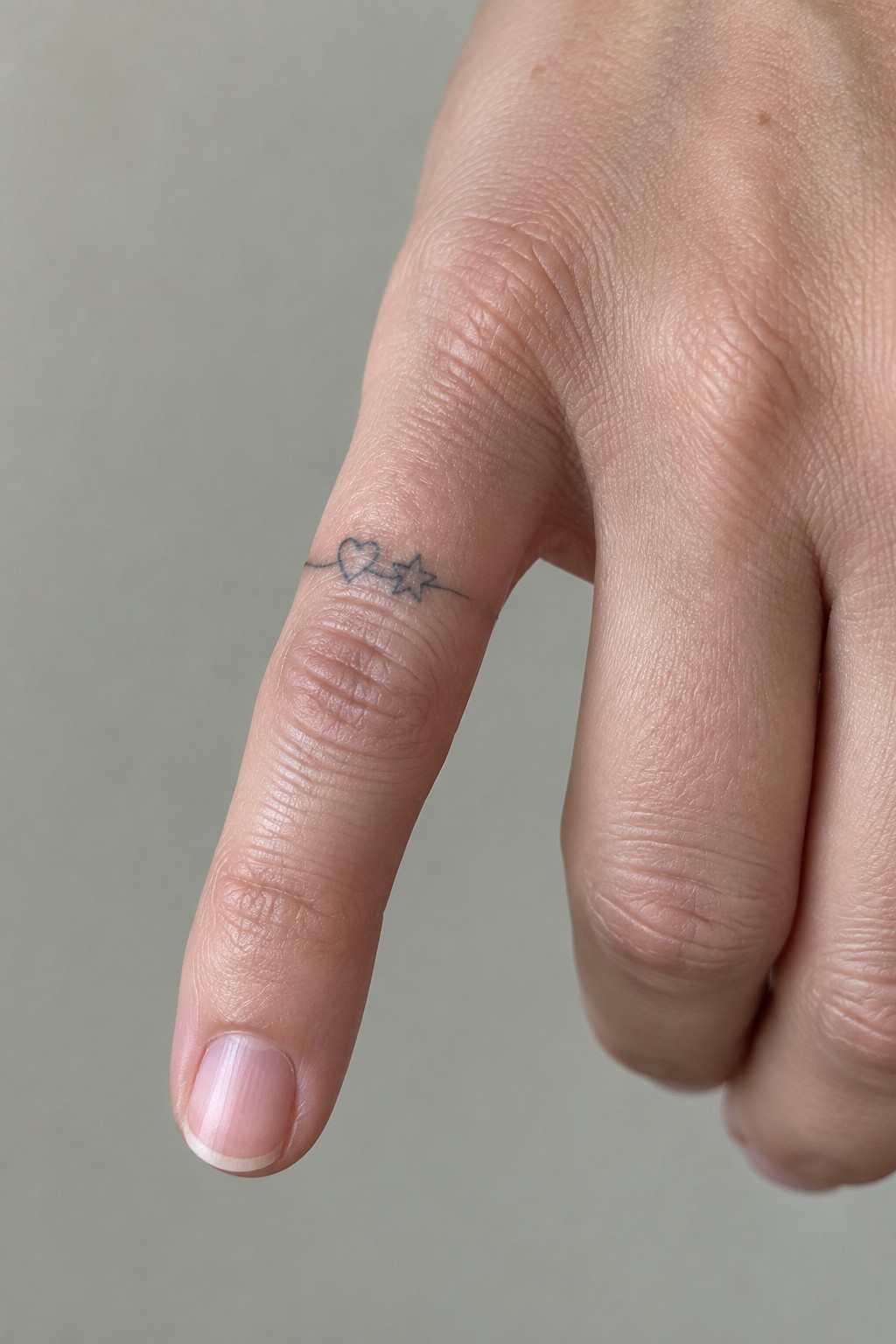 Close-up of finger with thin black line tattoo of heart and star.