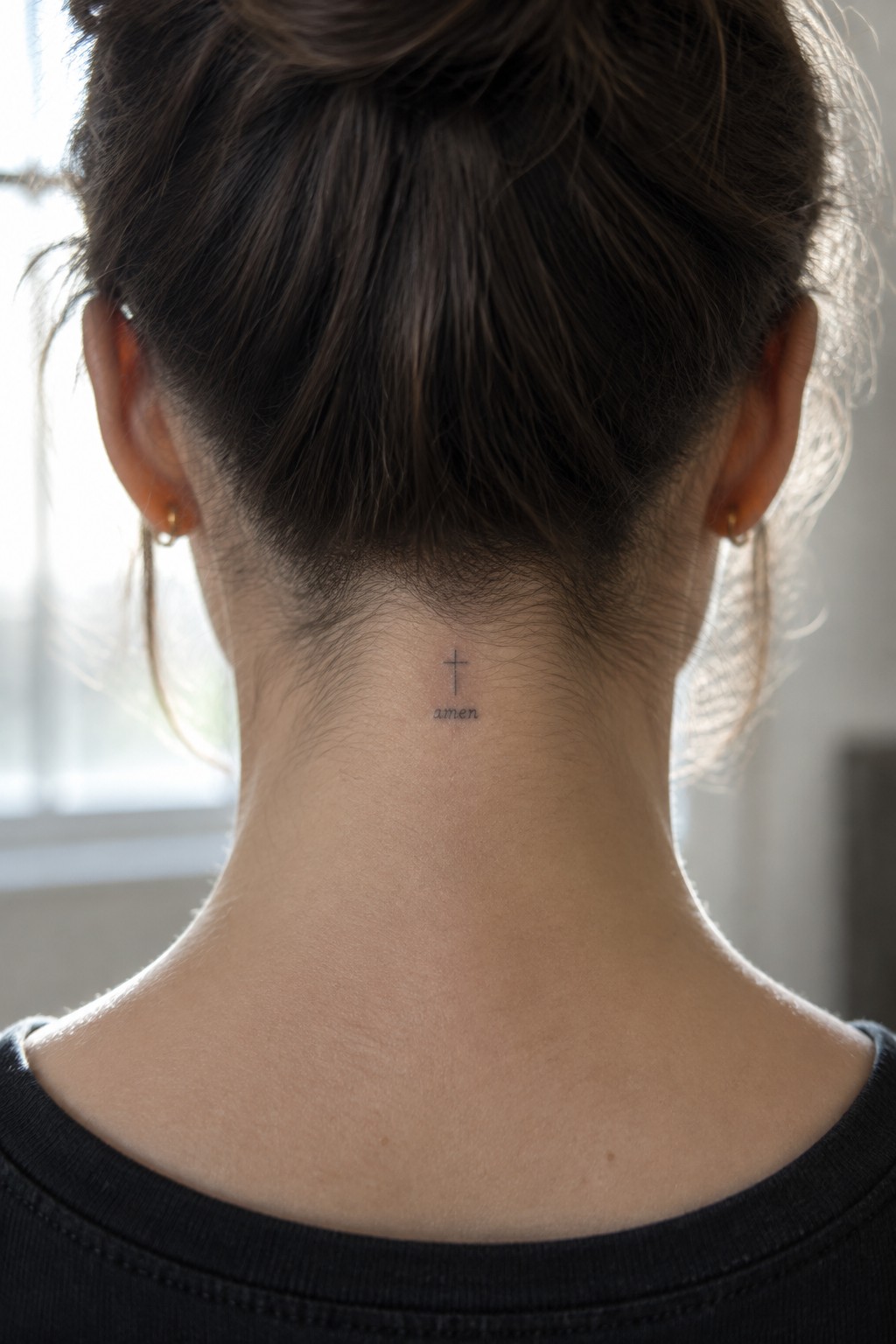 Woman's neck with cross and amen tattoo below bun and gold hoop earrings