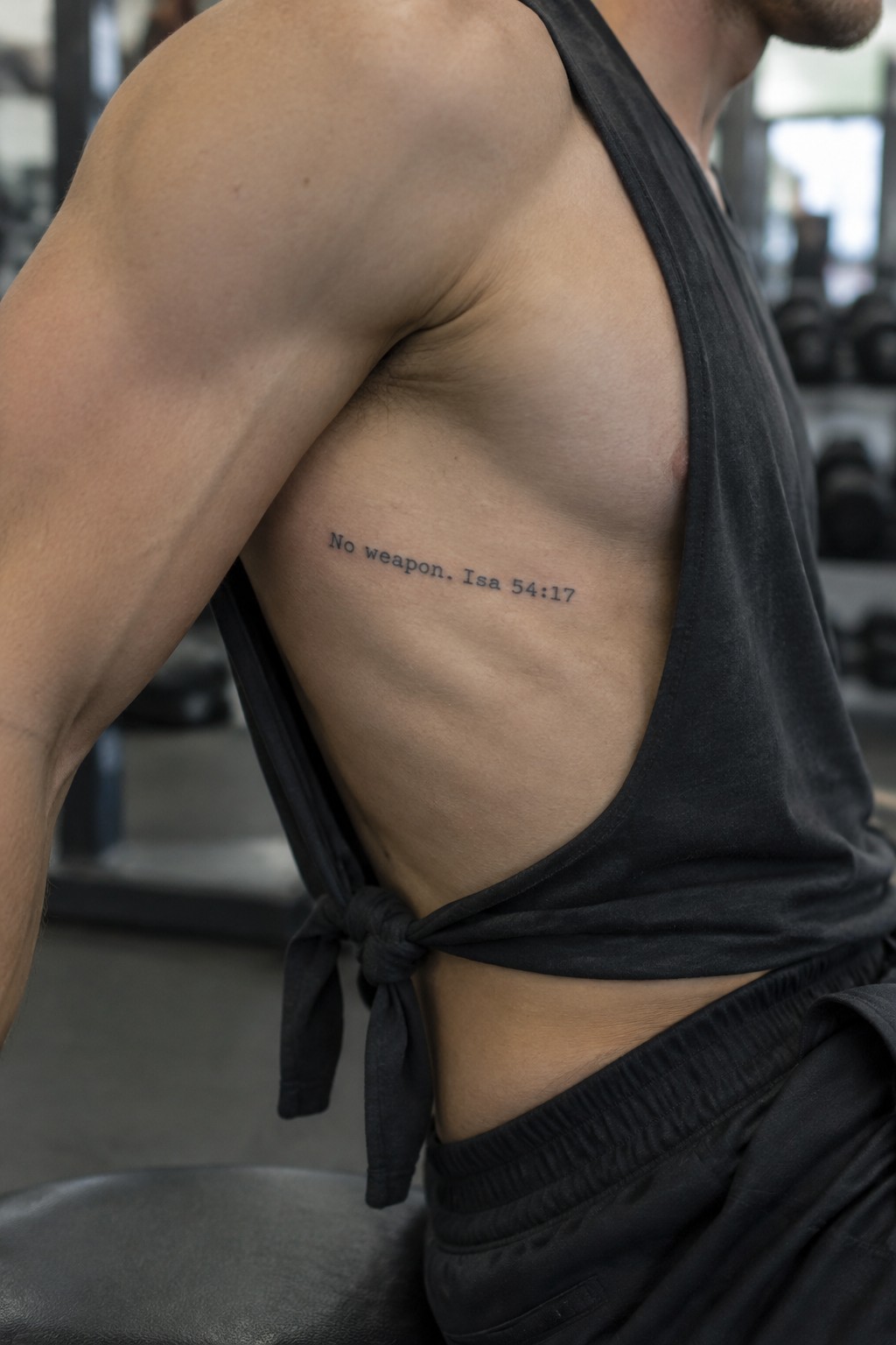 Muscular man with rib tattoo in knotted black tank top at gym