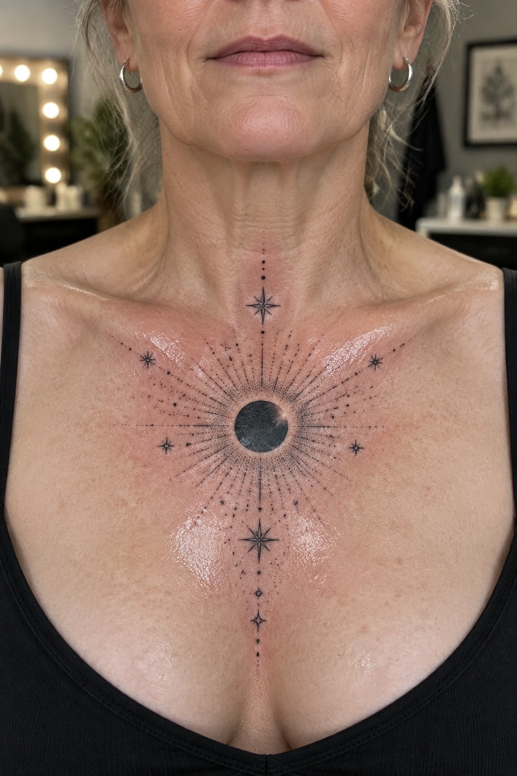 Woman's chest with large black sunburst tattoo, central circle, rays and stars.