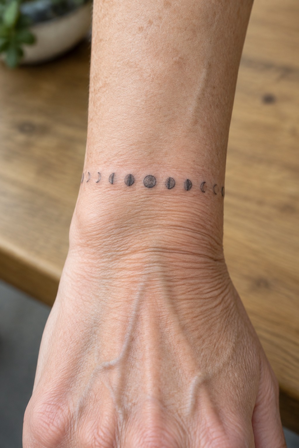 Wrist with moon phases tattoo on wrinkled skin over wooden table