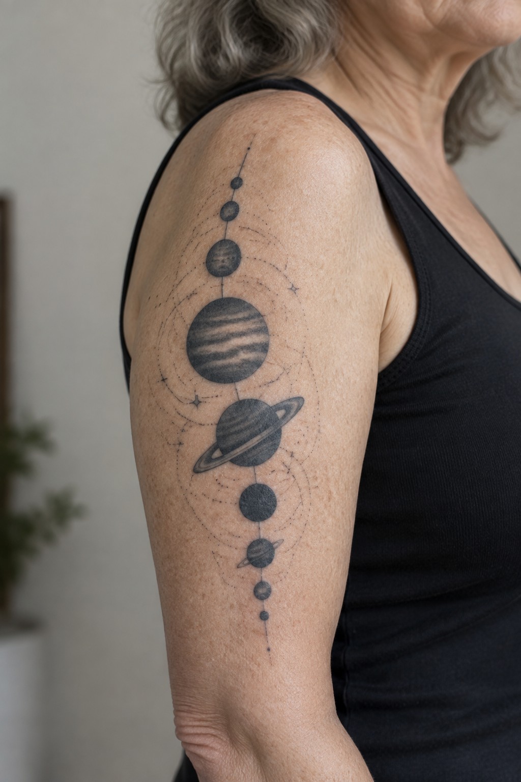 Black tank top with vertical solar system planet tattoo on older person's shoulder