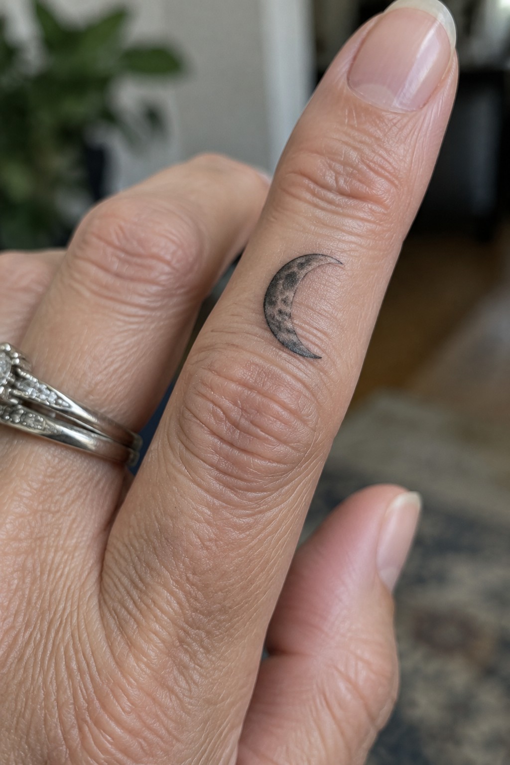 Small crescent moon tattoo with dotted shading on the side of a finger