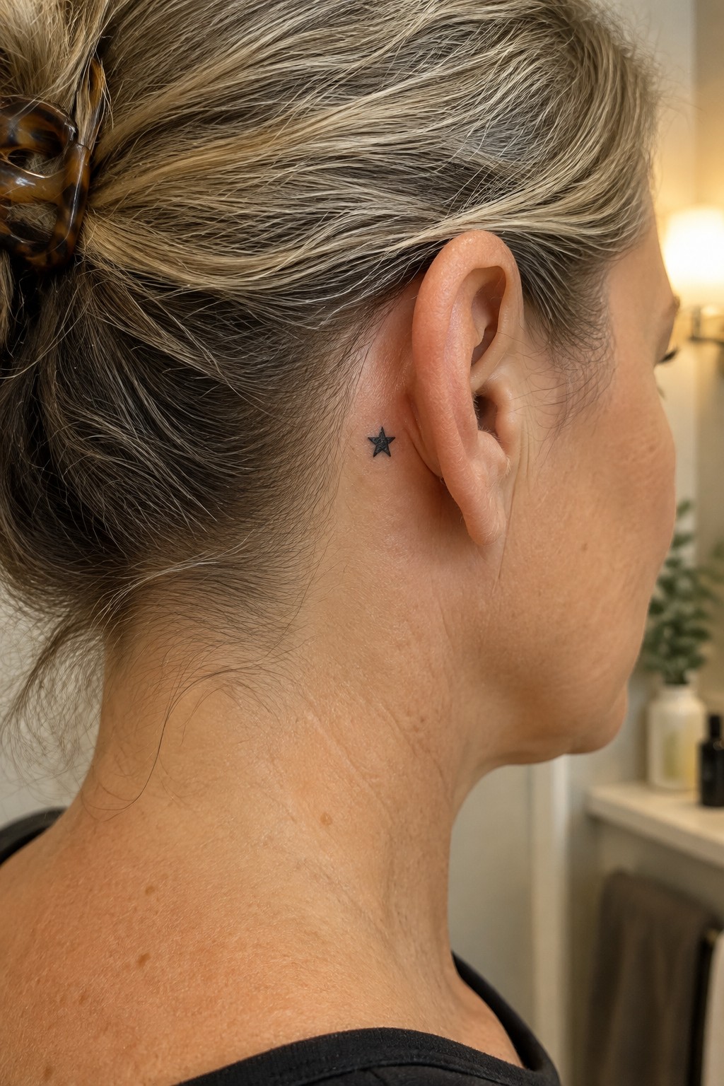 Blonde woman in black top with small star tattoo behind ear