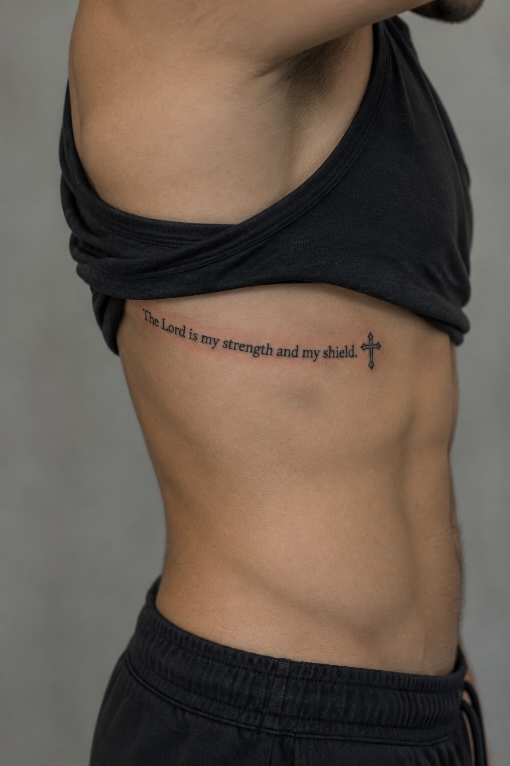 Black script tattoo on the side of a man's torso reading 