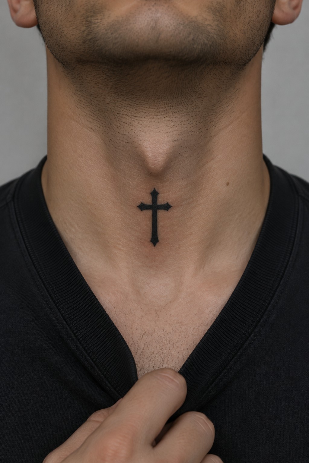 Man's neck with black cross tattoo, hand pulling black V-neck shirt down