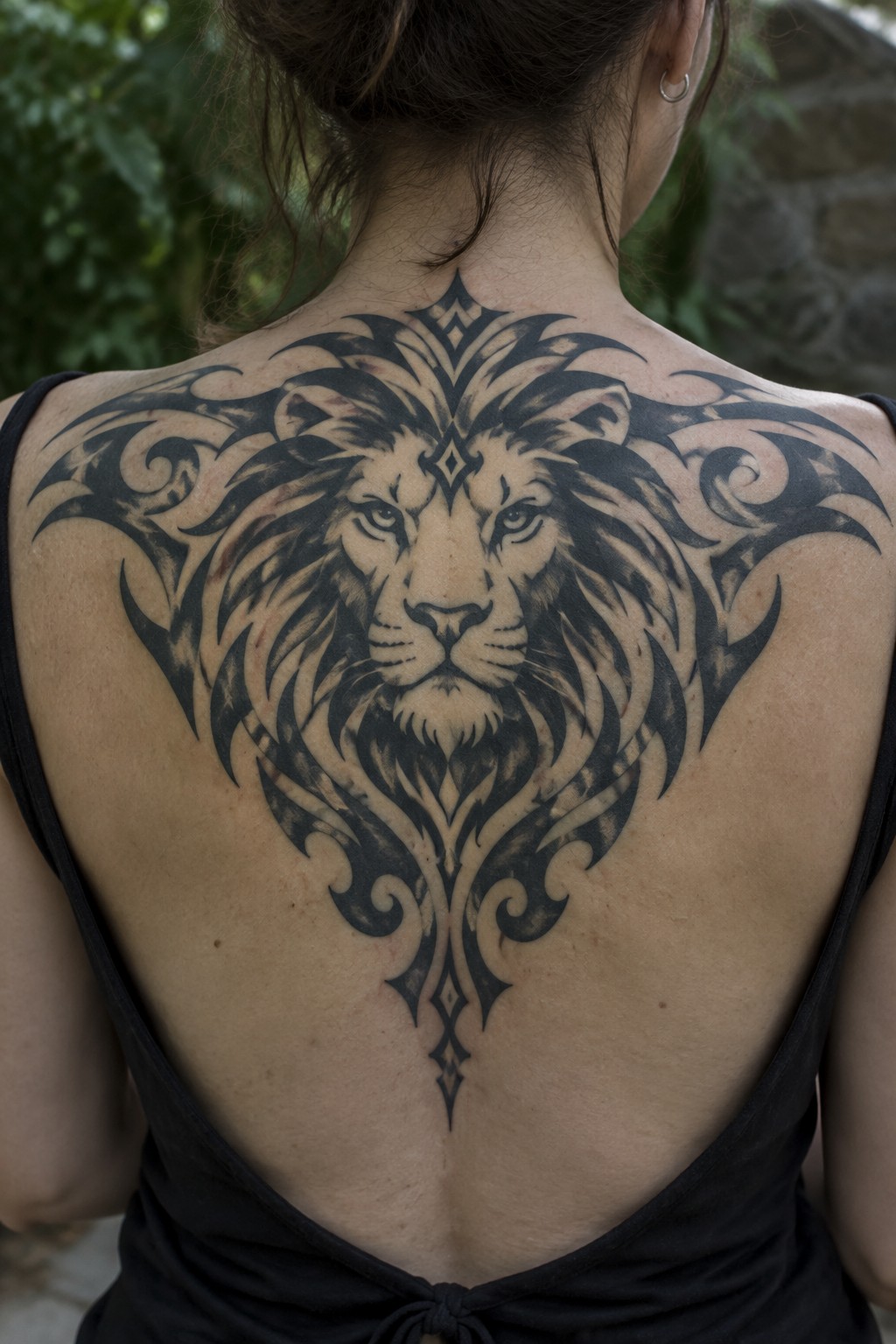 Woman's back with large ornate black lion tattoo and tribal patterns