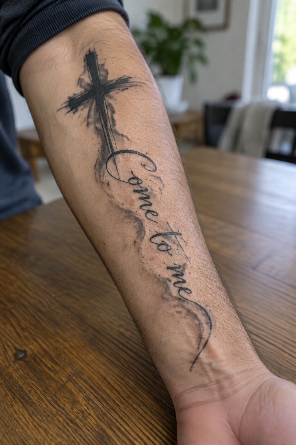 Forearm tattoo of a brushstroke cross above the cursive text 