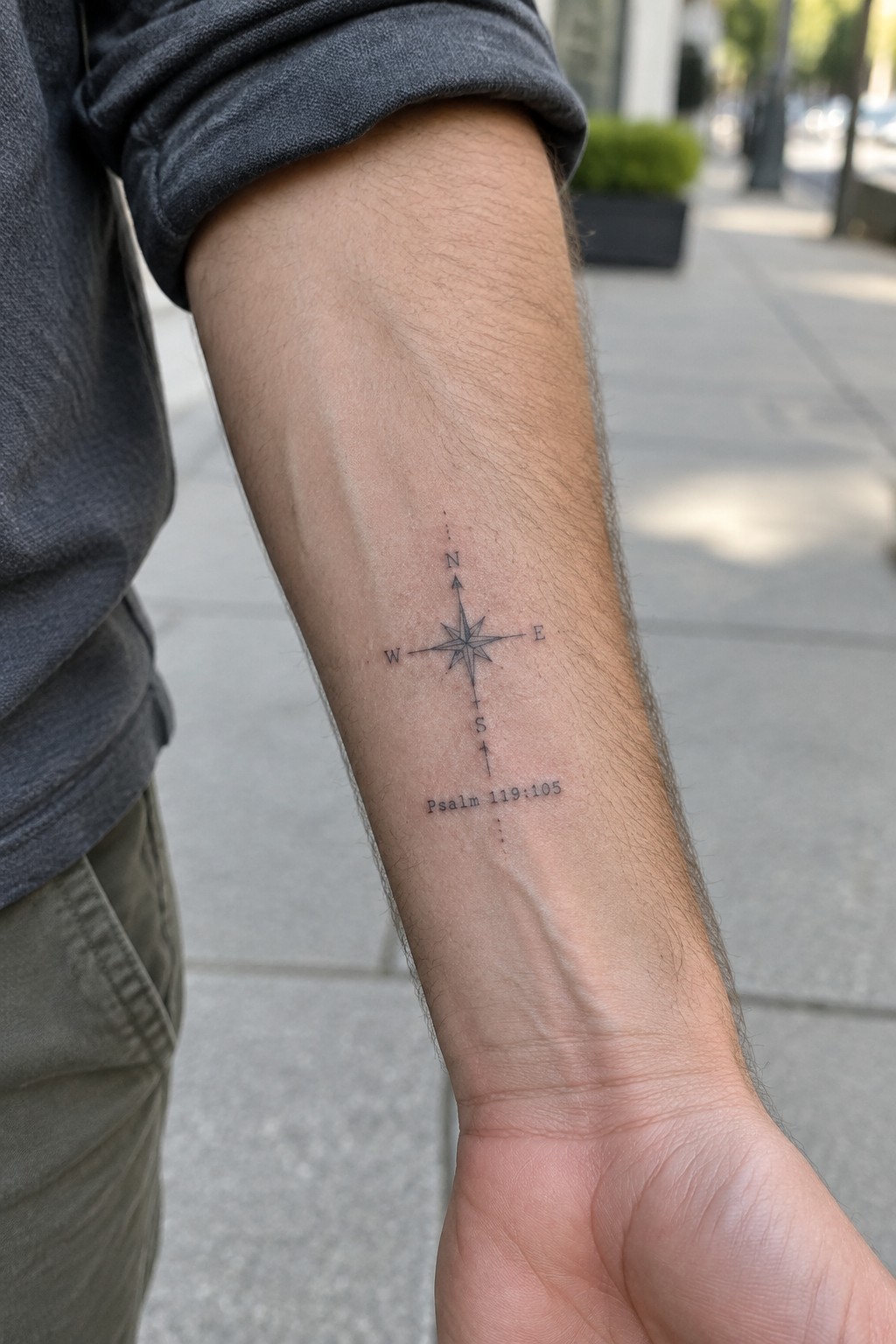 Gray sleeve rolled up on forearm with compass tattoo and Psalm 119:105