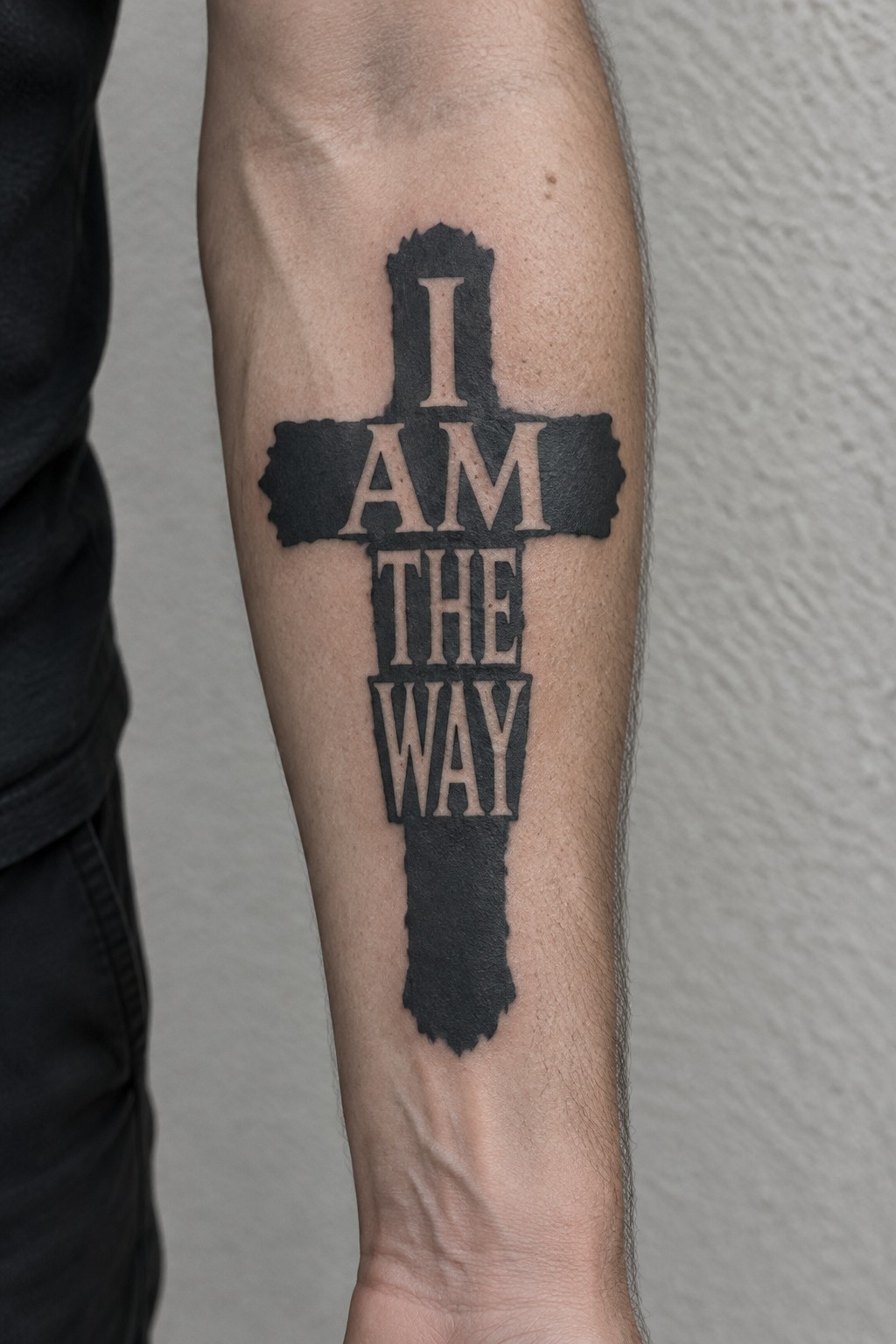 Black cross tattoo on forearm with beige text 