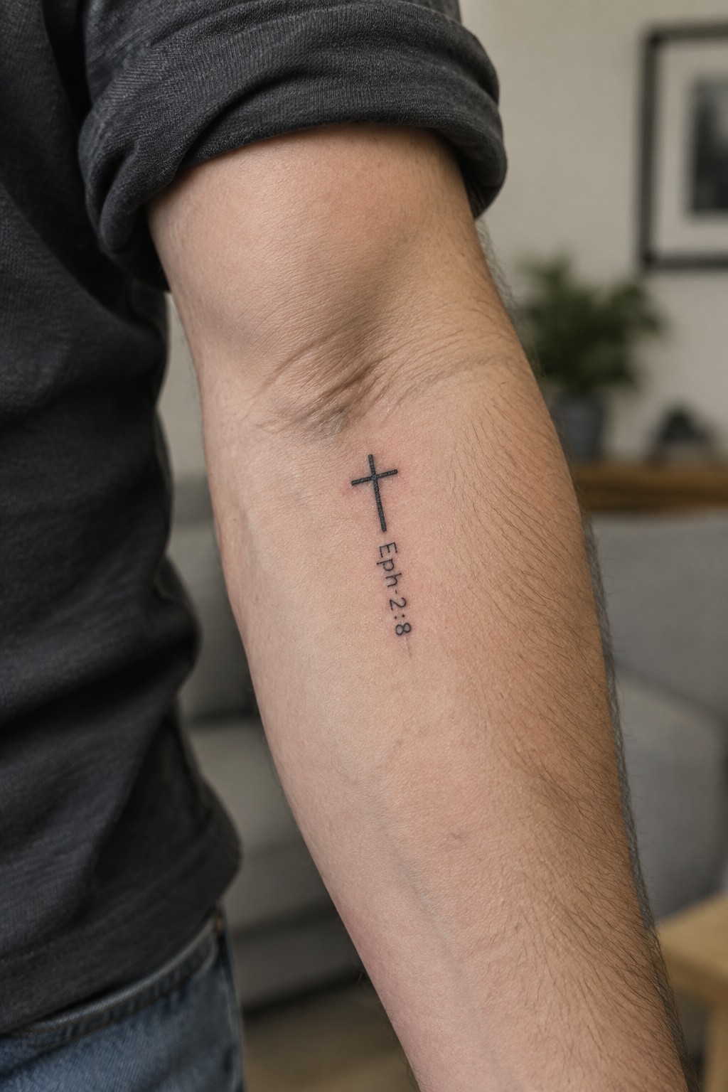 Small black cross tattoo with Eph. 2:8 text placed vertically on the inner forearm