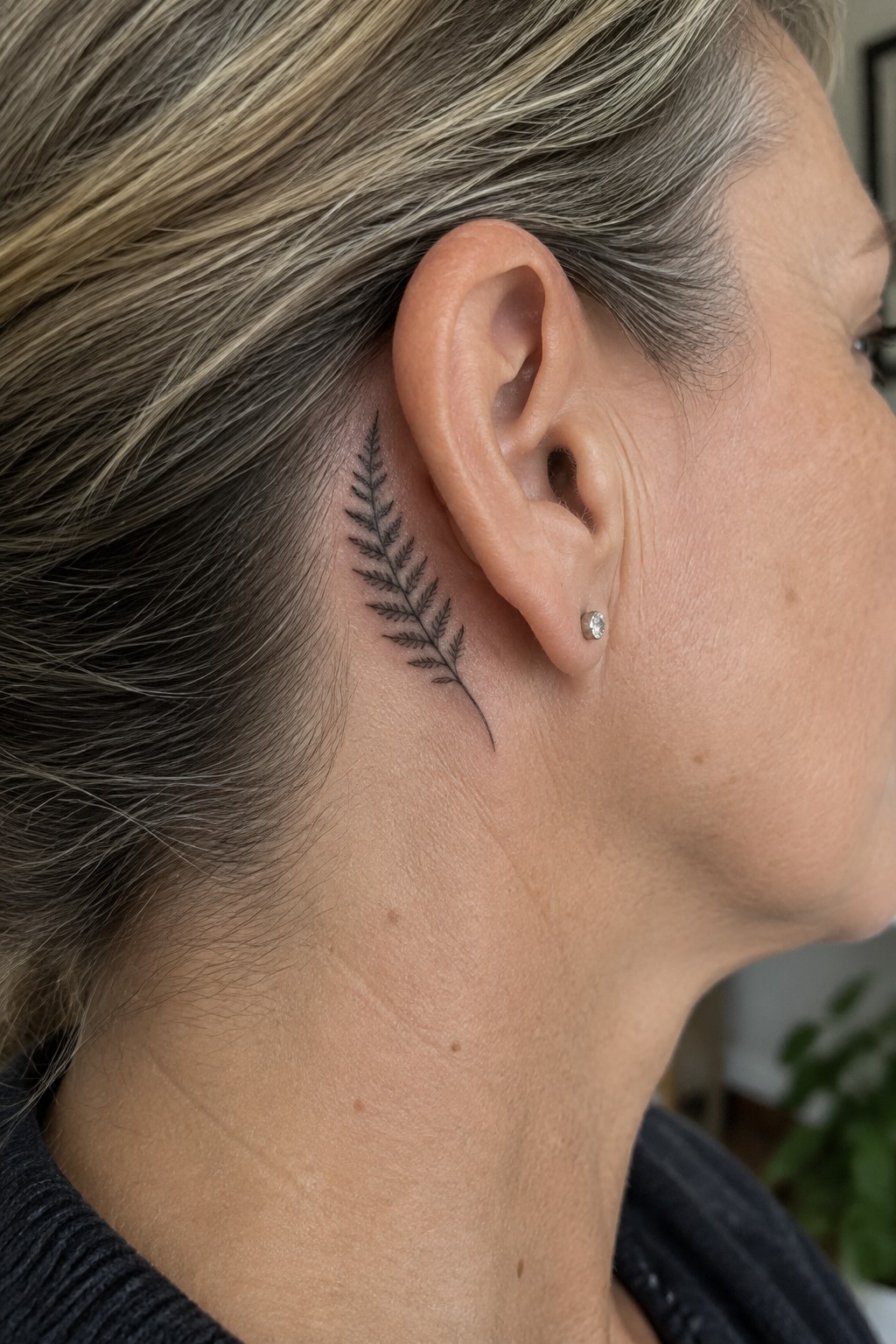 Fern tattoo behind woman's ear beside small diamond stud earring