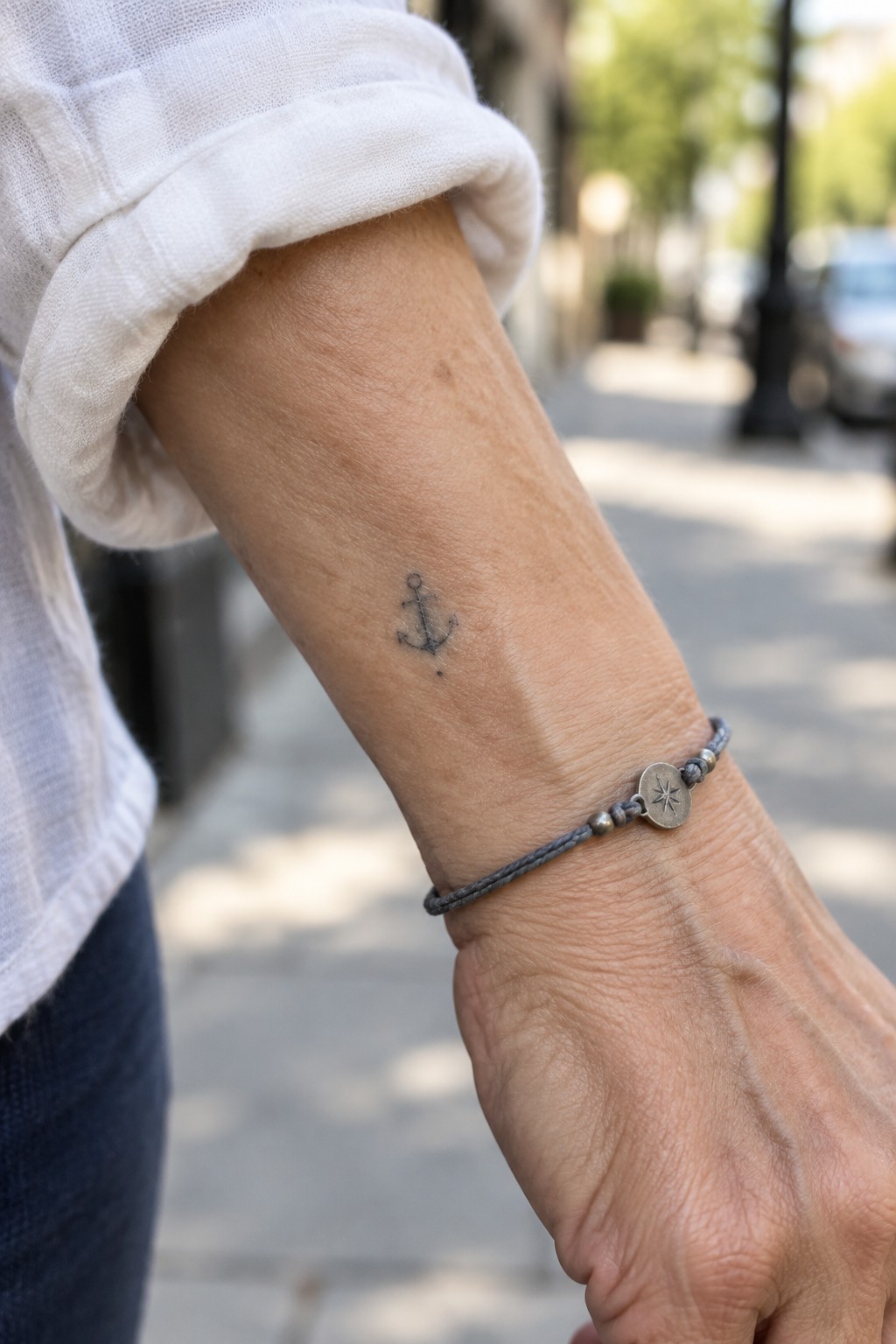 Rolled white sleeve over anchor tattoo and gray star-charm bracelet on wrist
