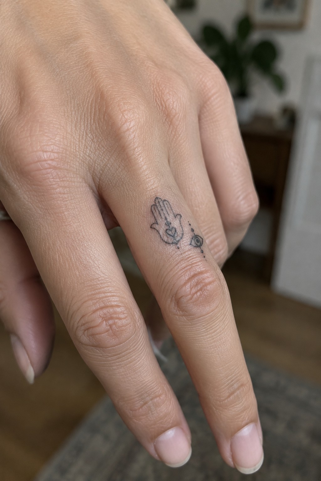 Hand's ring finger with small black hamsa heart and eye tattoo