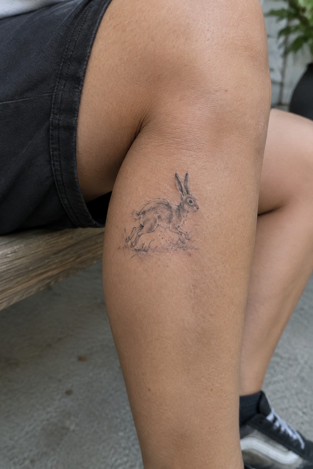 Fine line tattoo of a running rabbit on the outer thigh with grass details below it