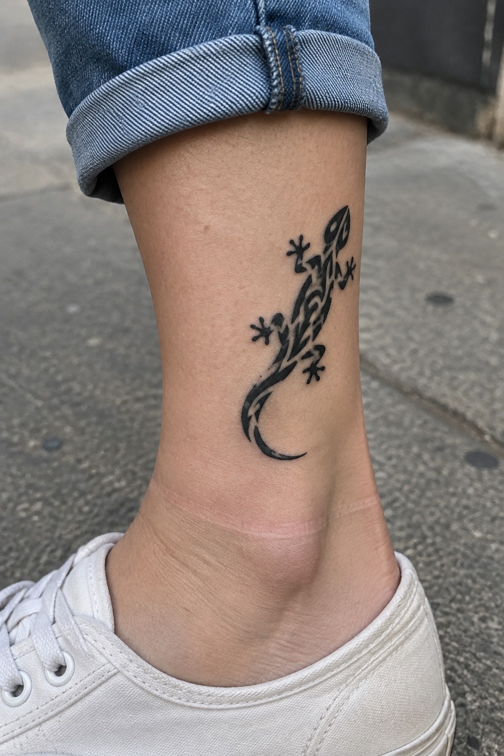 Black tribal lizard tattoo on ankle above white sneaker and cuffed jeans