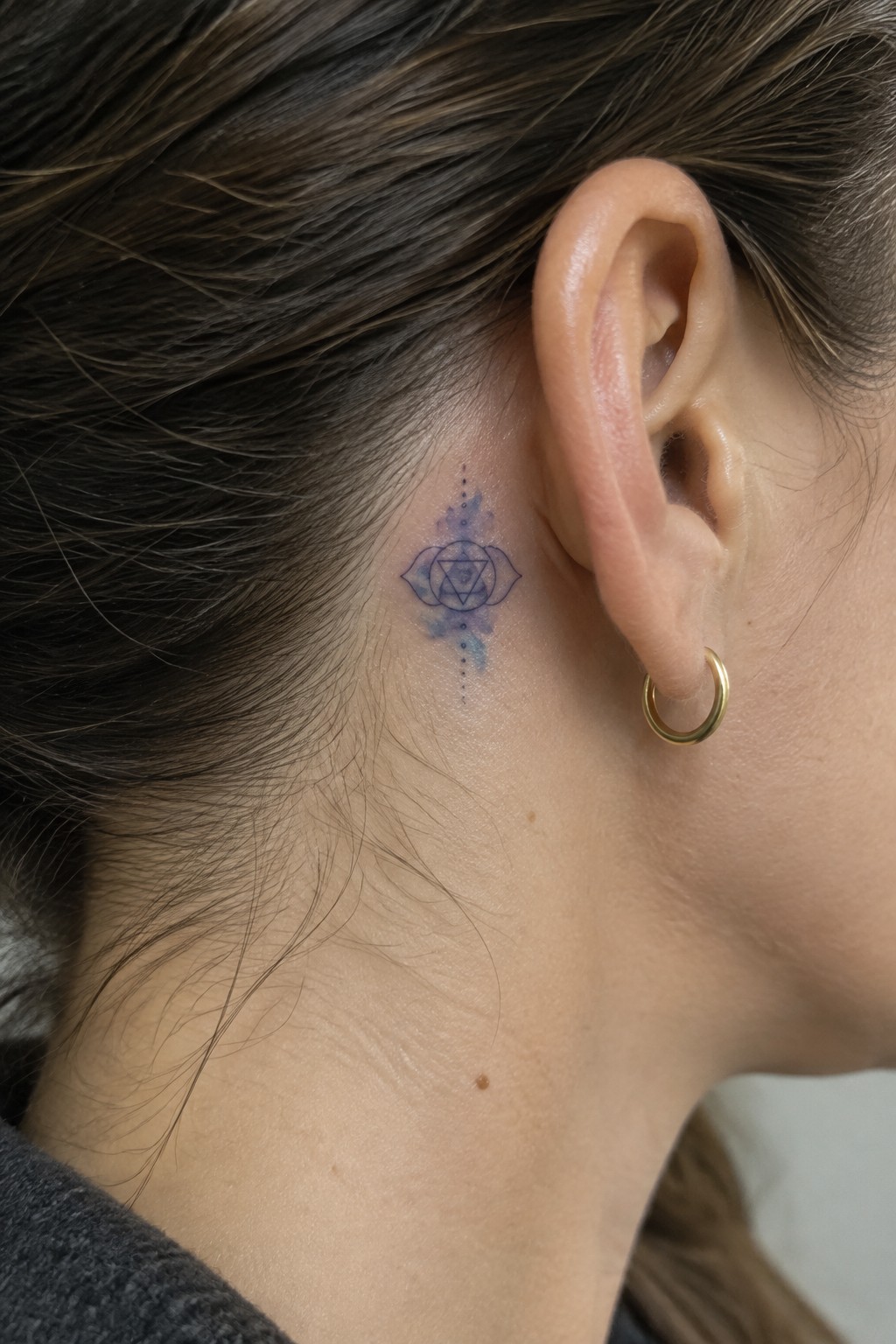 Neck tattoo with blue geometric star, lotus petals, and watercolor accents beside gold hoop earring.