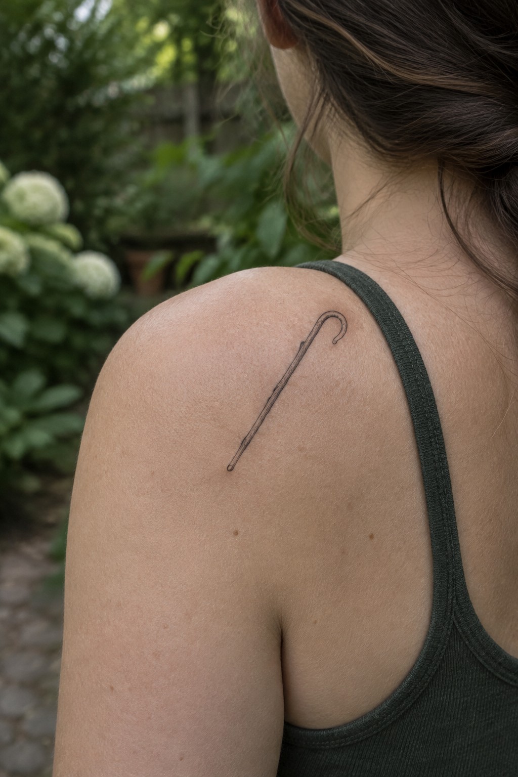 Woman's shoulder in dark green tank top with black shepherd's crook tattoo