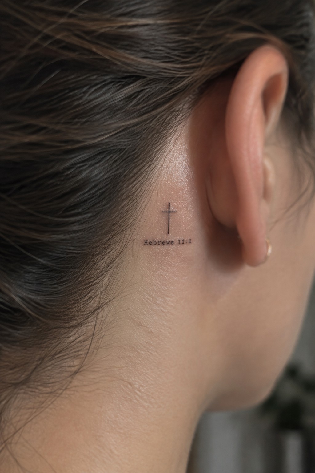Small cross tattoo with Hebrews 11:1 text behind a person's ear