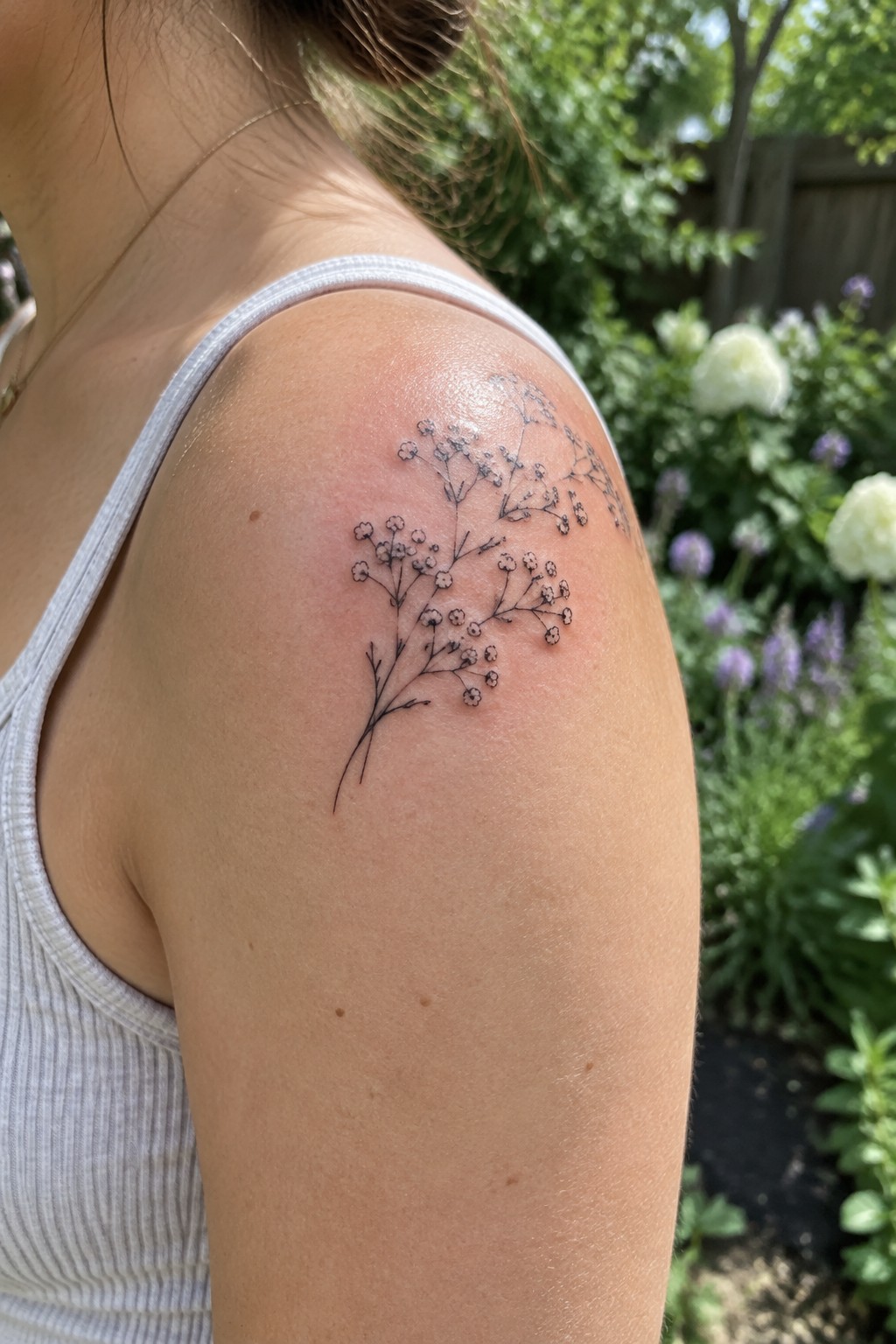 Delicate black baby's breath tattoo on shoulder above white tank top in garden