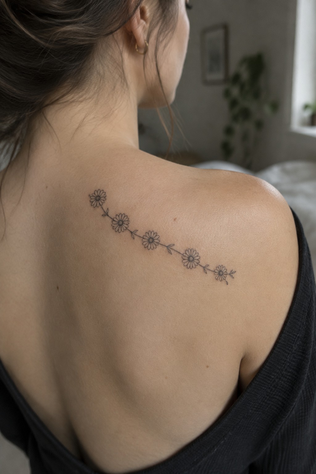 Woman's bare shoulder with curving black daisy flower tattoo above dark top