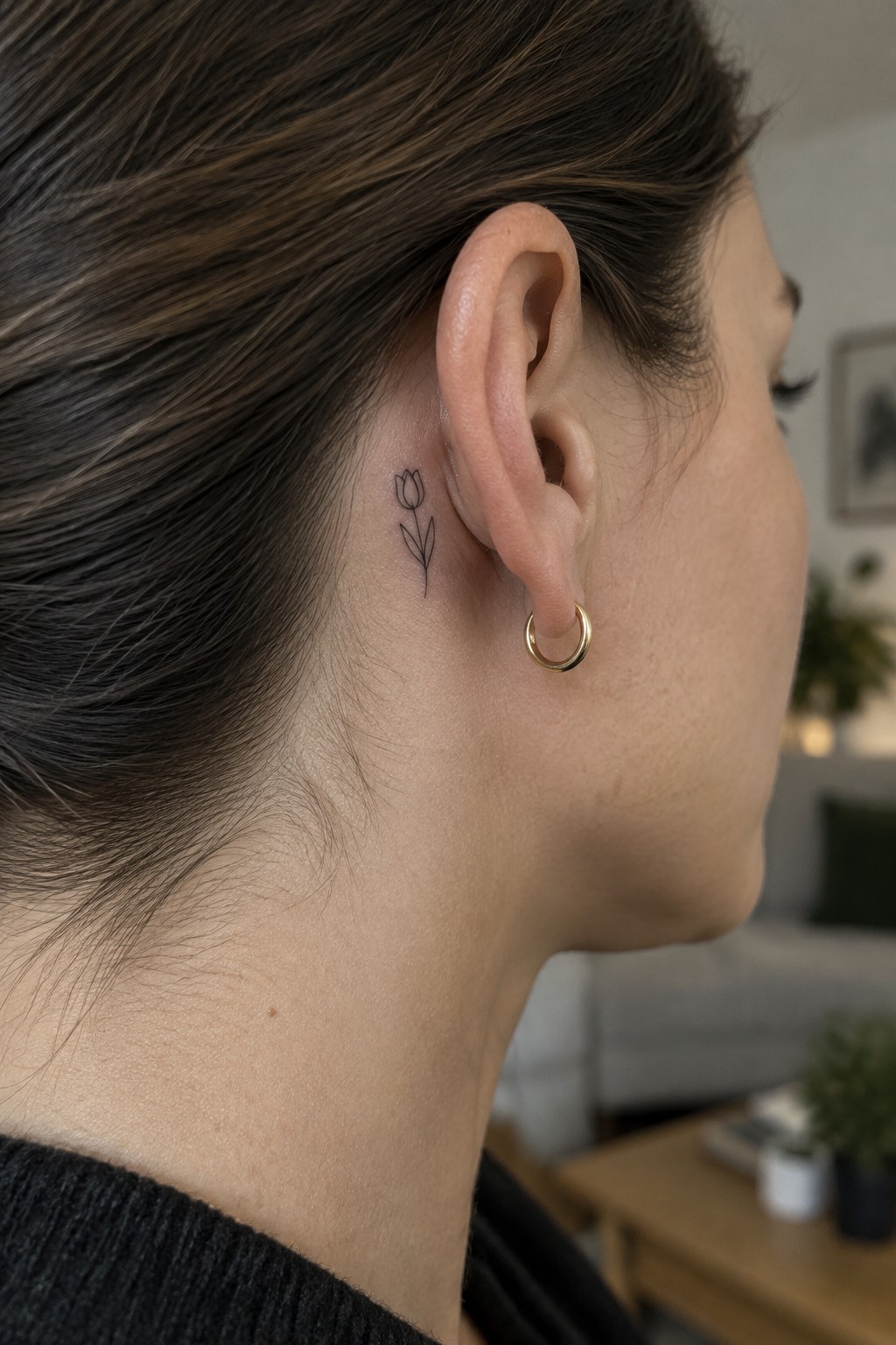 Small fine line tulip tattoo positioned behind a woman's ear on the side of her head.