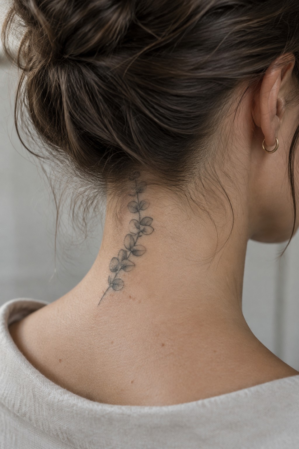 Woman's neck with leafy vine tattoo, dark hair in bun, light top