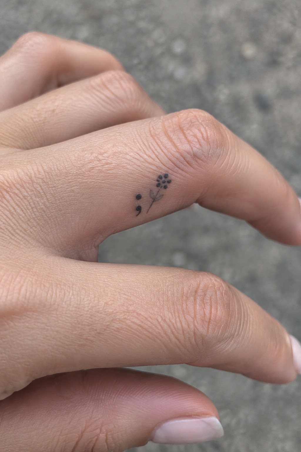 A tiny black fine-line flower sprig tattoo on the side of a finger, with dotted blossoms and a slim stem.