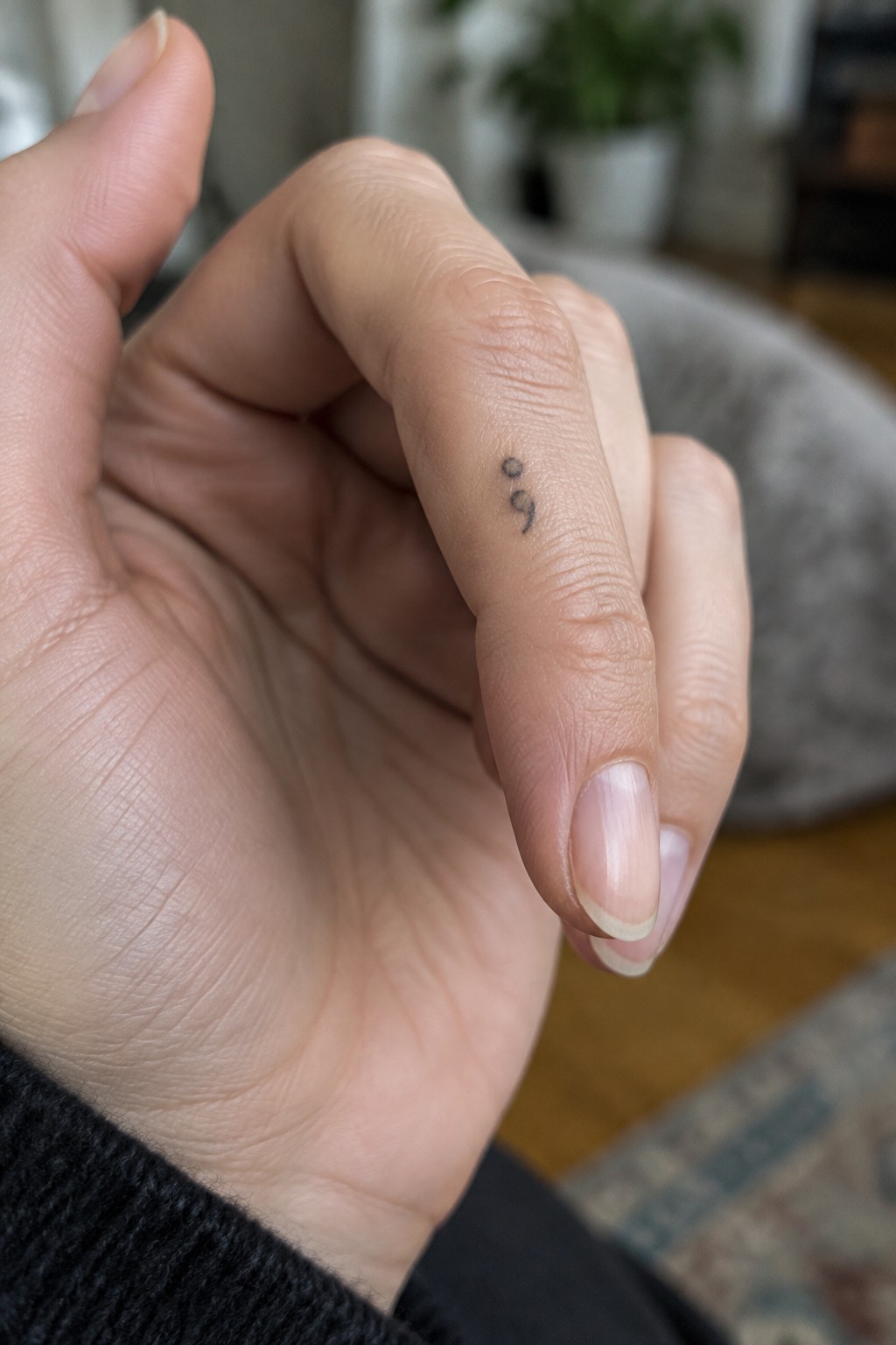 Tiny black semicolon tattoo on the side of a finger.