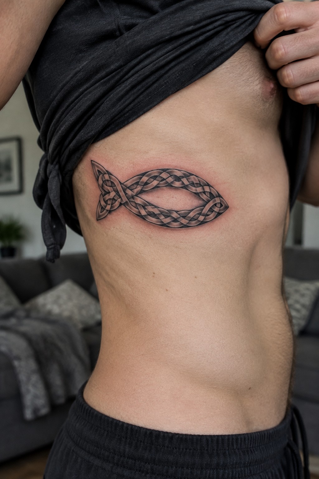Person lifting black shirt to show intricate Celtic knot fish tattoo on side