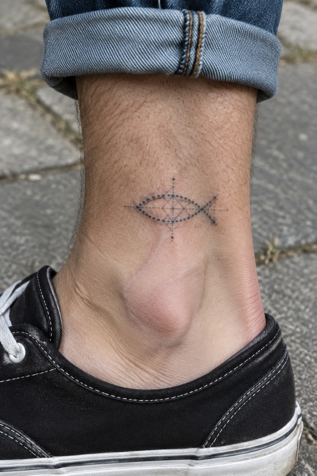 Geometric dotted fish tattoo on ankle above black sneaker with rolled jeans