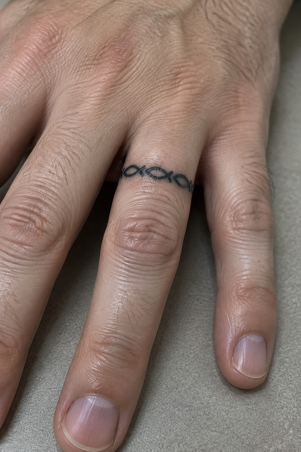 Close-up of light-skinned hand with black linked fish tattoo on ring finger.