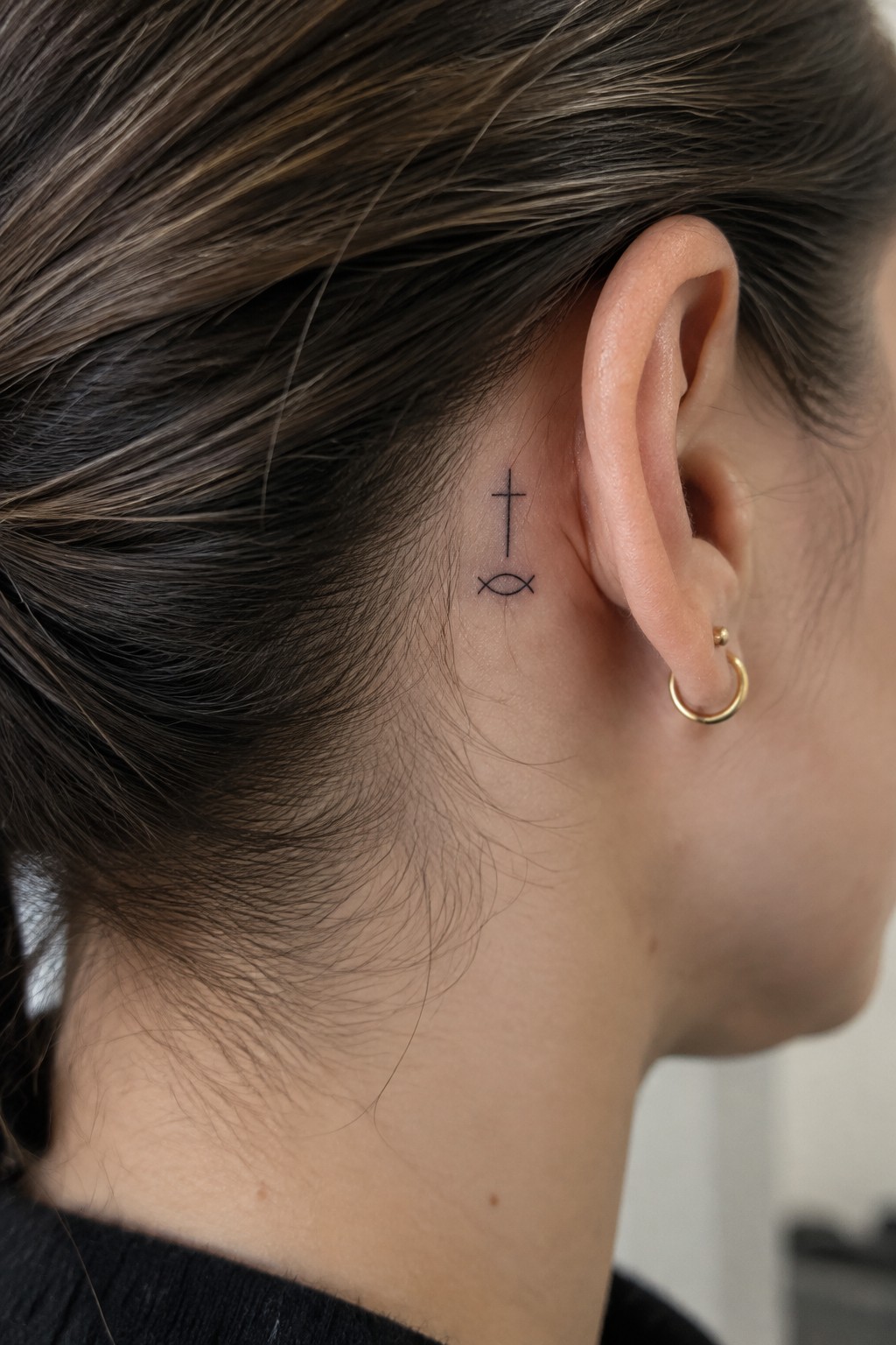 Cross and fish tattoo behind ear with brown hair and gold hoop earring