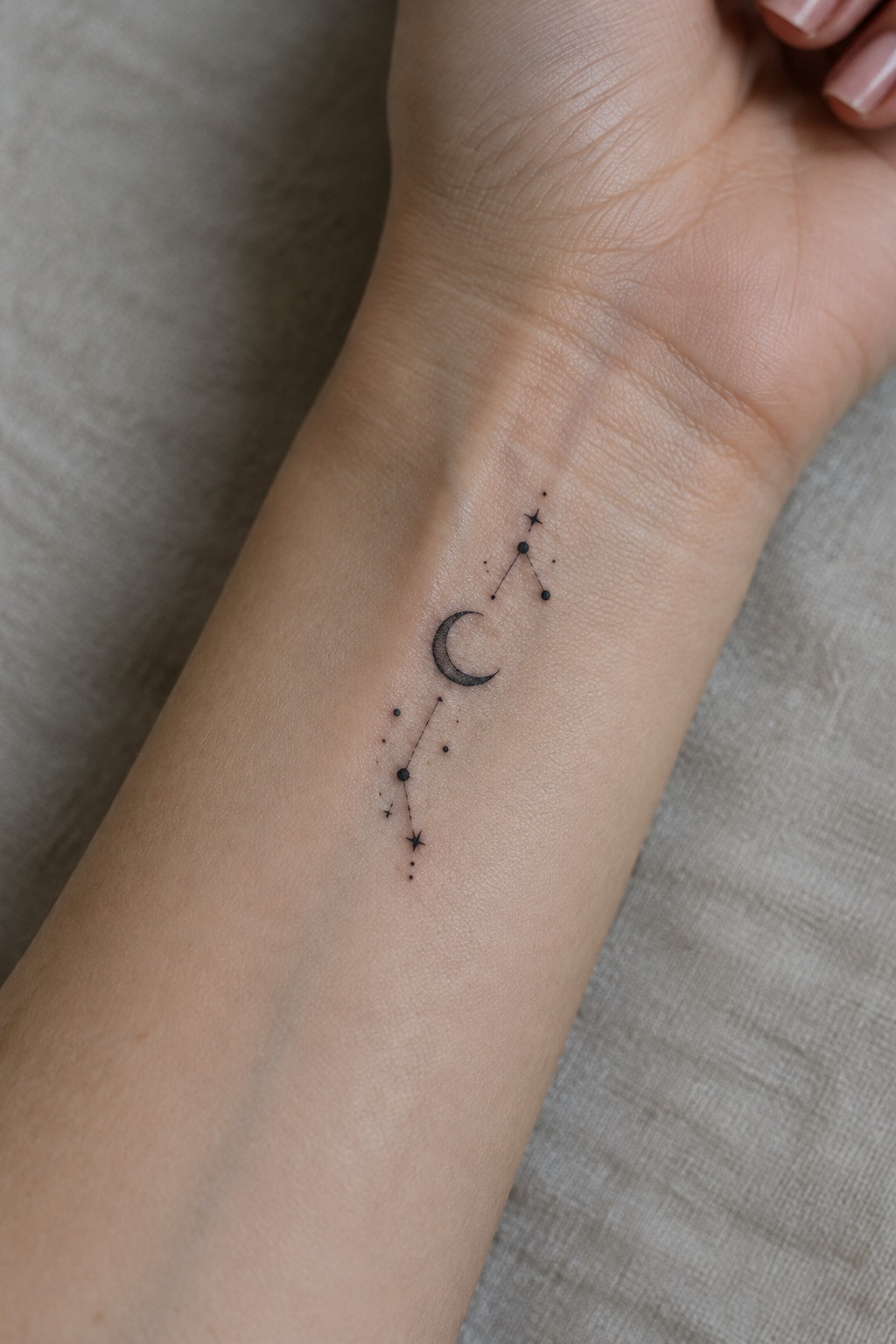 Small black crescent moon and star constellation tattoo running vertically along the inner wrist.