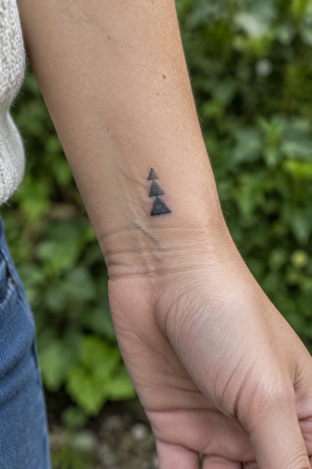 Three small black triangles stacked vertically as a tattoo on the inner wrist.