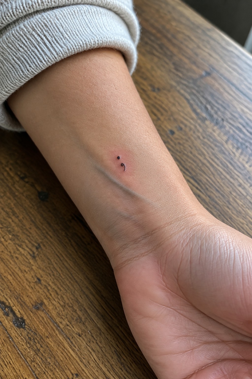 Small black semicolon tattoo on the inner wrist, with slight pinkness around the ink.
