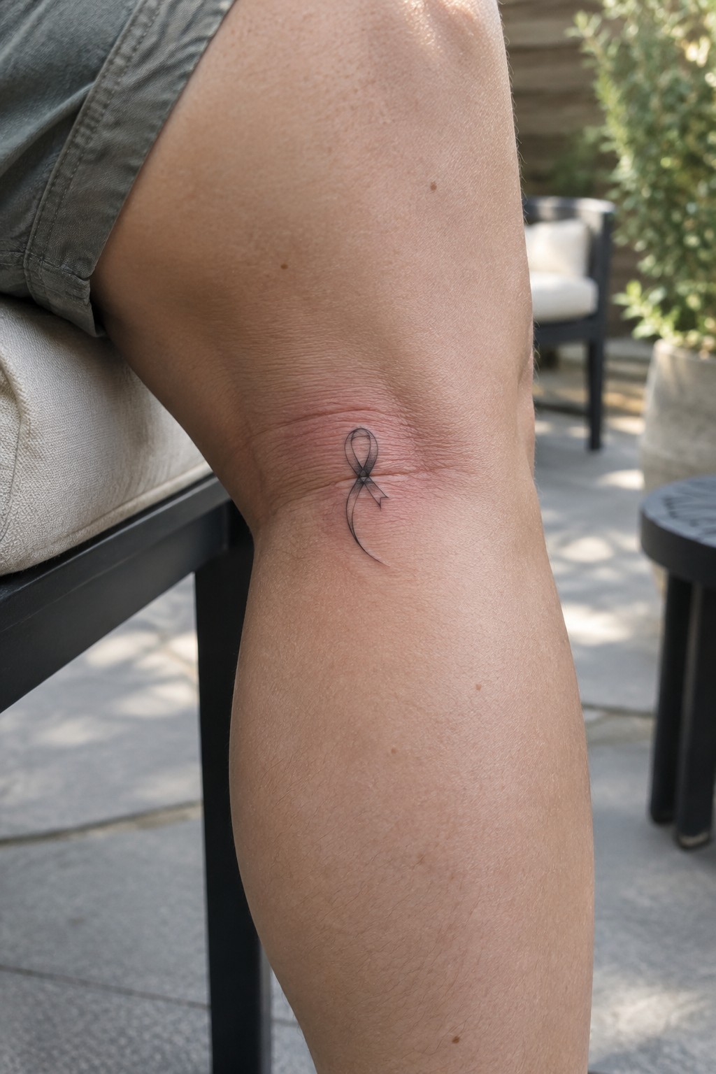 Black ribbon tattoo on reddened knee below gray shorts on outdoor patio