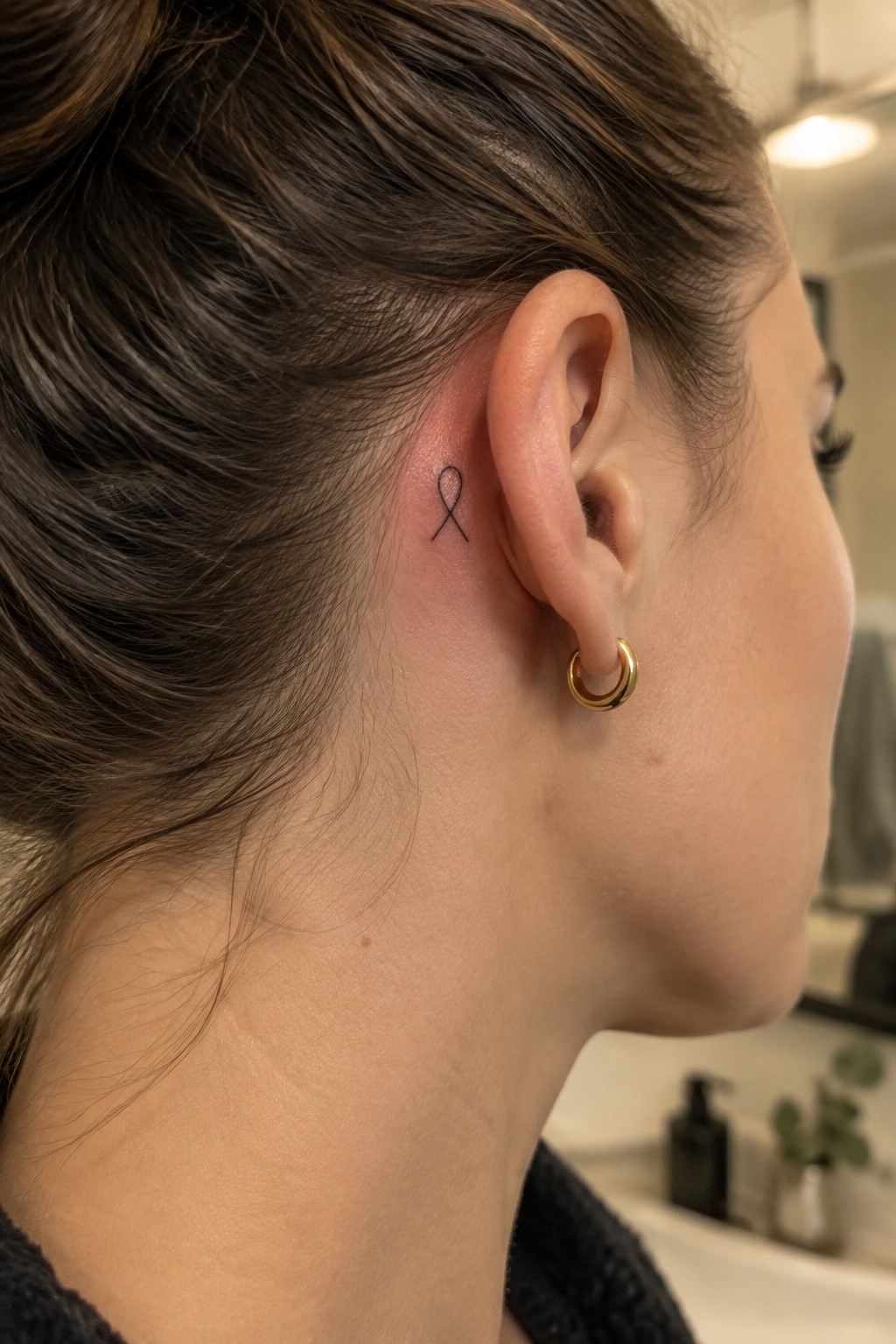 Small black ribbon tattoo behind the ear near the hairline
