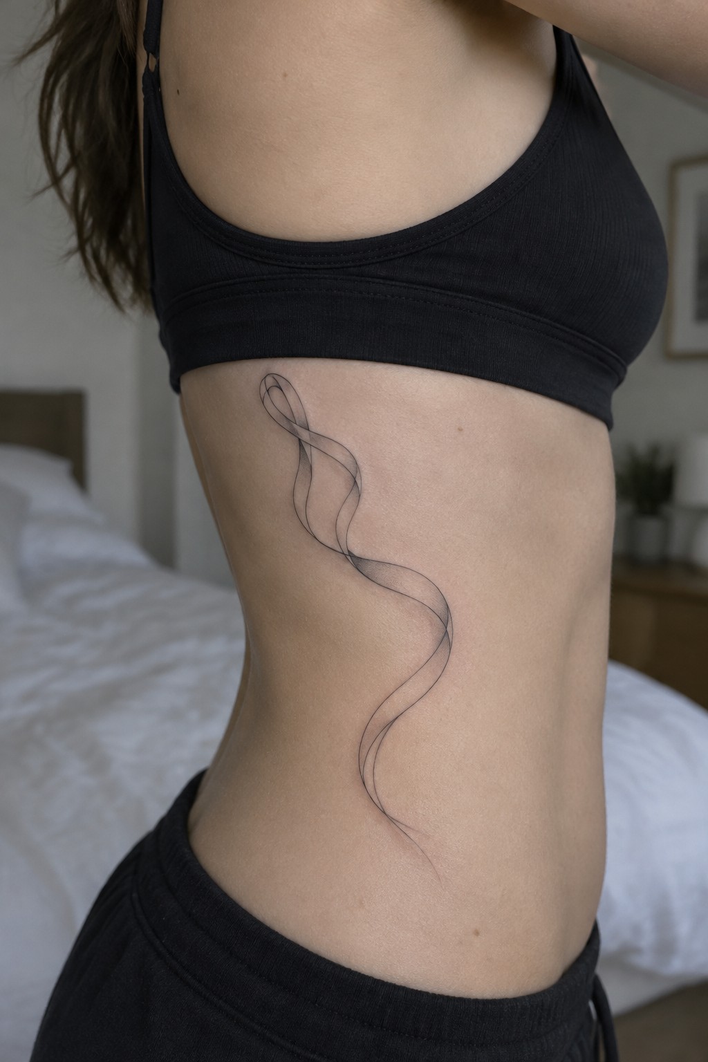 Woman's side torso with flowing black ribbon tattoo under black crop top